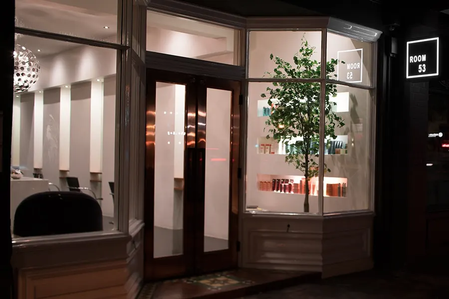 Room 53's shopfront at night, glass doors between lit white bay windows